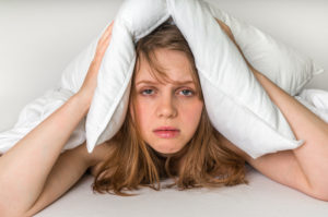 Young woman in bed covering ears with pillow