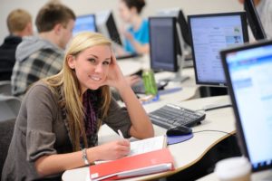 Student smiling sitting in a computer lab with other students.