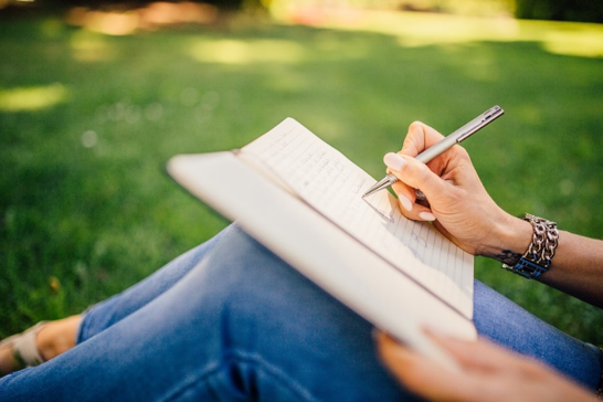 Image of book on a person knees while she is writing outdoors on a sunny day.