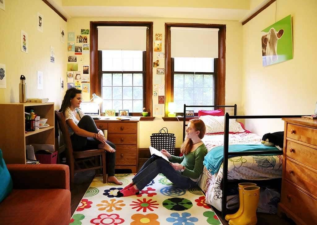 Two students inside dorm room talking.